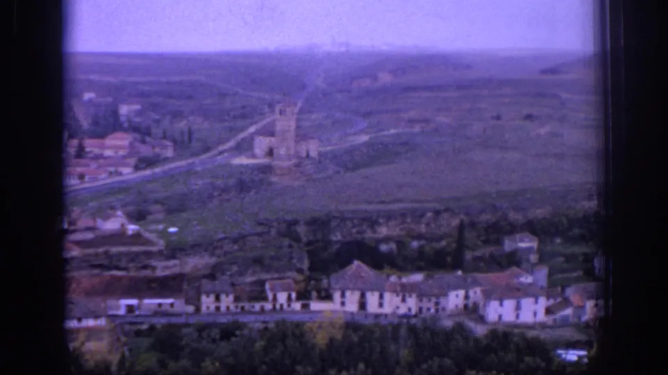 1966 Spain 8mm view of a distant village with a stone church tower, low buildings, roads, and open countryside.