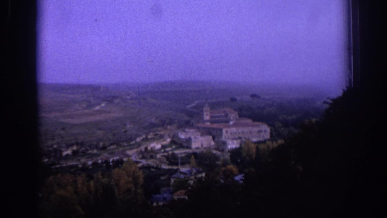 1966 Spain home-movie frame showing a church complex on a wooded rise, with fields and haze in the distance.