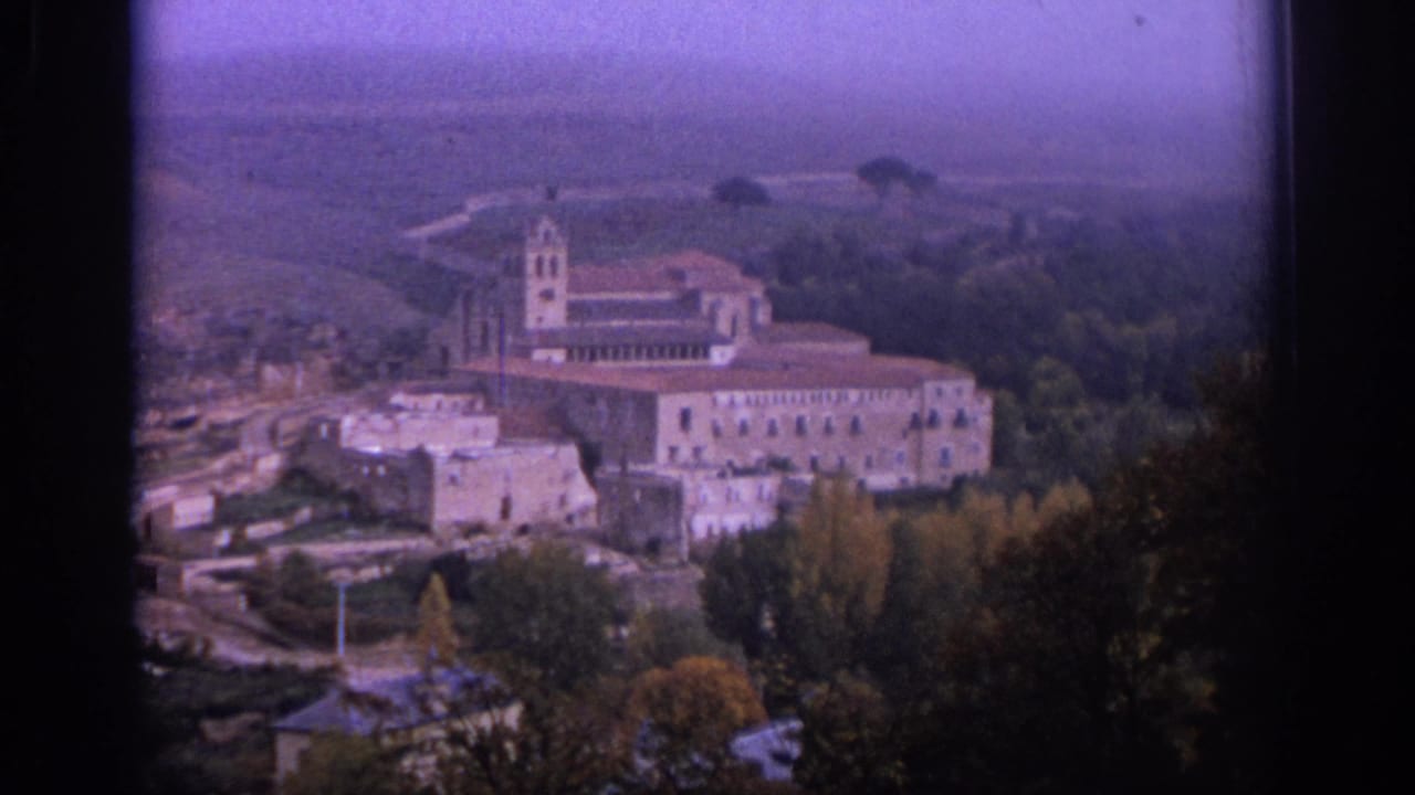1966 Spain home-movie view of a historic stone building complex set among trees on a hillside.