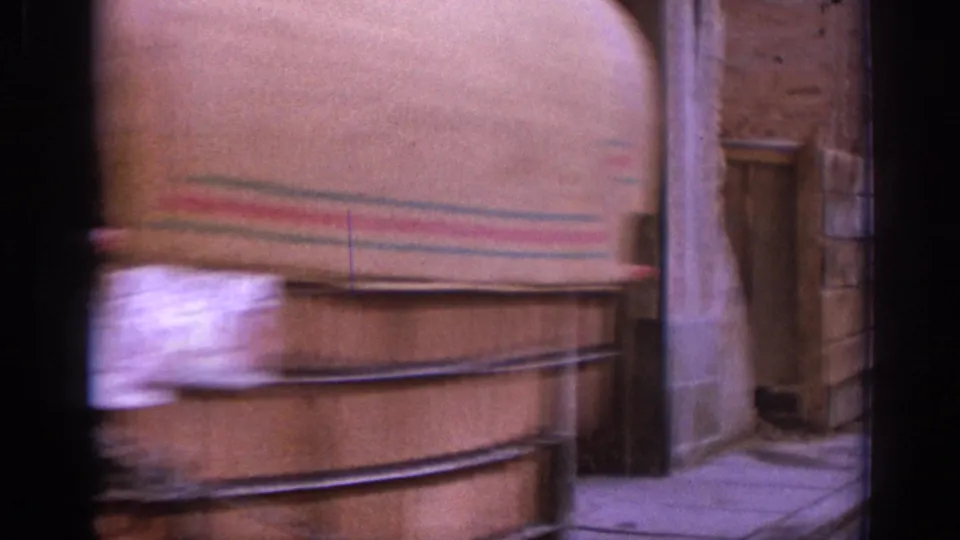 Motion-blurred 8mm frame showing the side of a passing carriage against a masonry street wall.