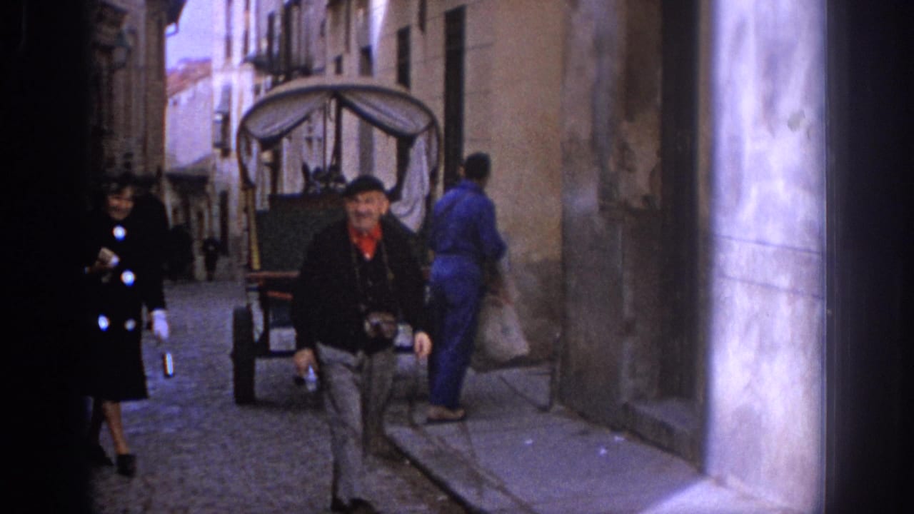 Man walks toward the camera near a covered cart and street pedestrians.