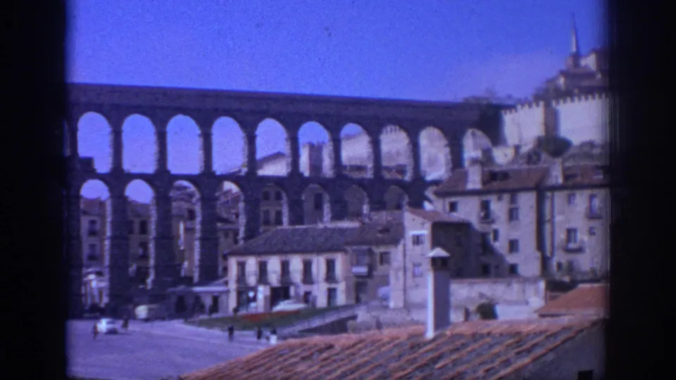 1966 Spain travel footage shows a large Roman aqueduct rising above buildings, roof tiles, and an open plaza.
