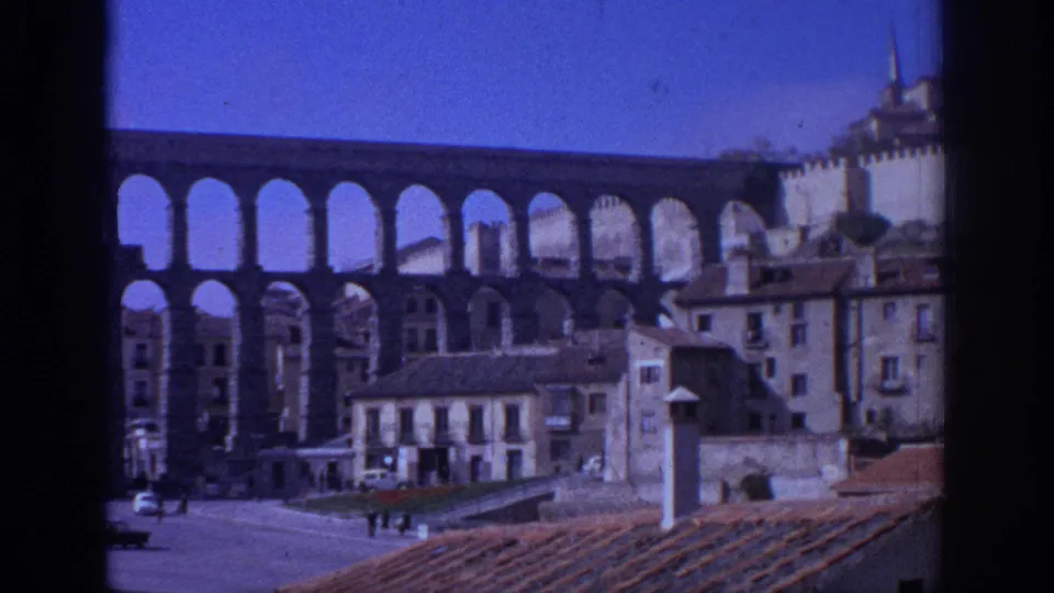 1966 Spain view of the aqueduct with repeated stone arches, town buildings, rooftops, and small distant figures.