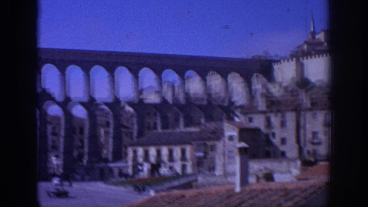 1966 Spain home-movie view of the Aqueduct of Segovia rising behind town buildings, seen through a dark window-like frame.