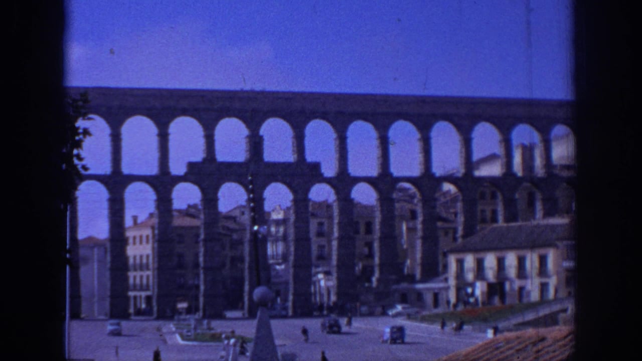 1966 Segovia town-square view with the aqueduct spanning the background, pedestrians and cars below, and buildings beneath the arches.