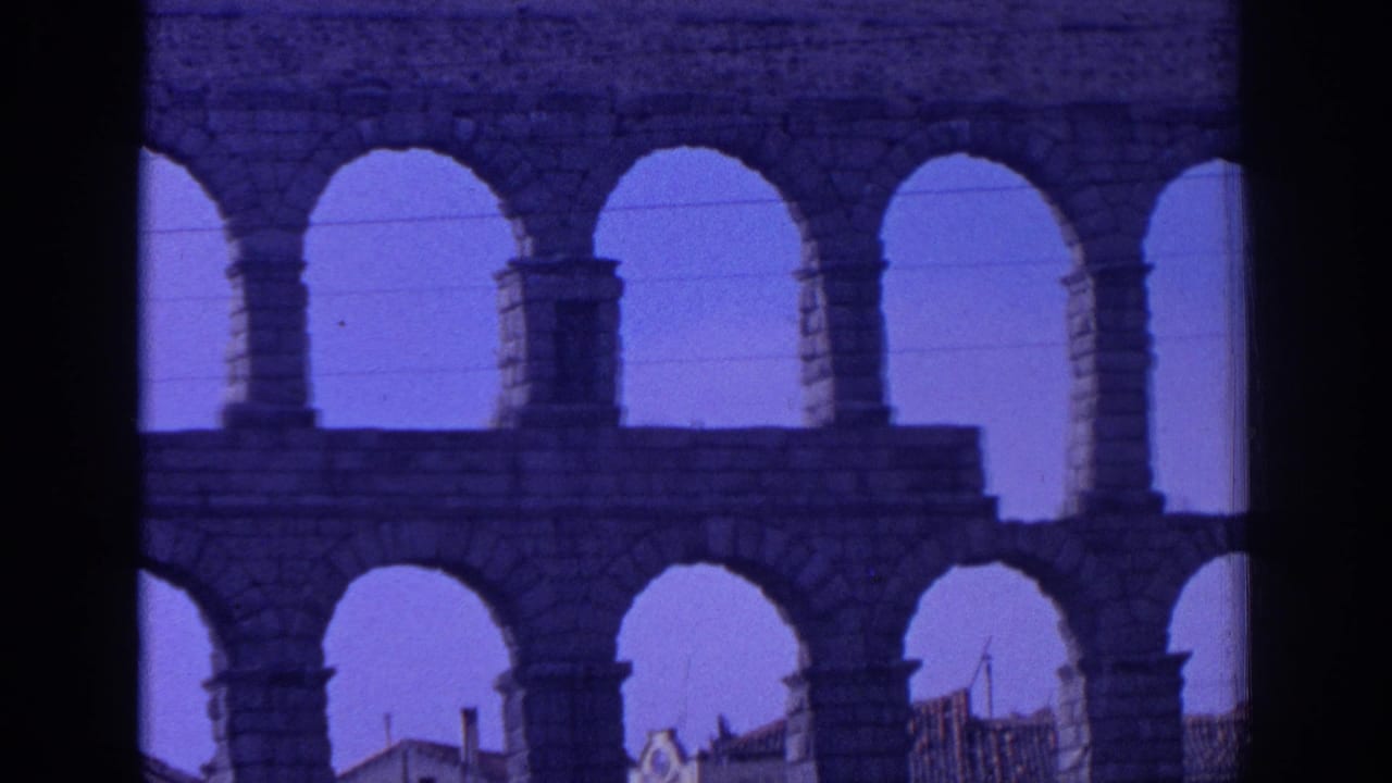 1966 Spain 8mm frame looking through Roman aqueduct arches with sky, power lines and dark scan borders visible.