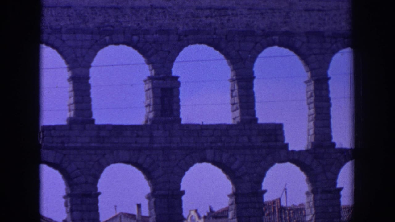 1966 Spain 8mm view through the aqueduct, showing repeated stone arches, tall piers and rooftops behind them.