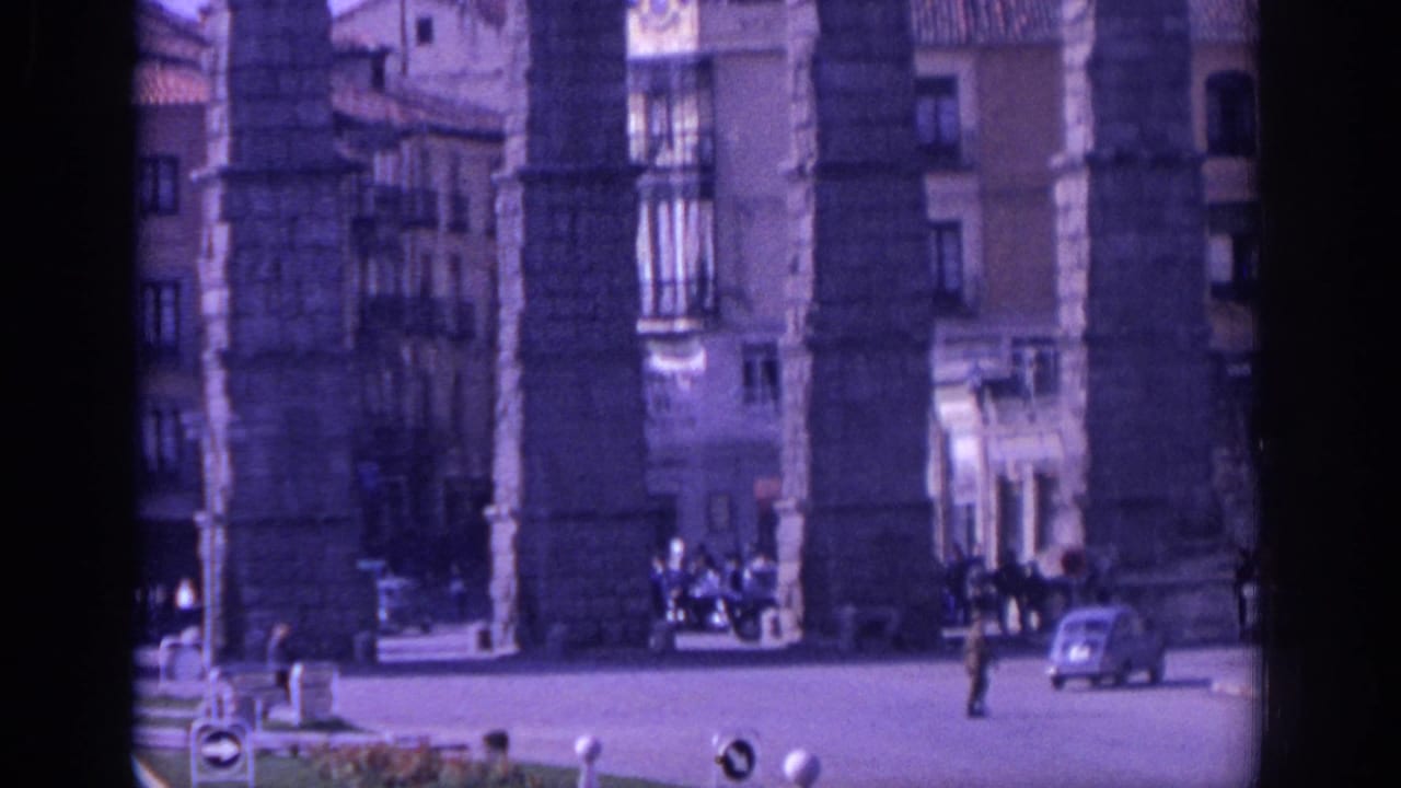 Large stone aqueduct piers beside a city street with cars and pedestrians.