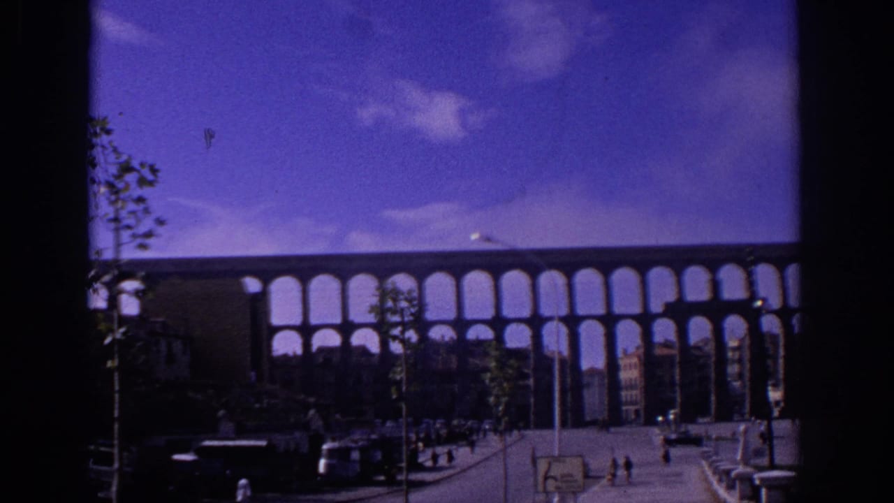 Aqueduct spans the background above a street with cars, pedestrians, trees, and buildings.