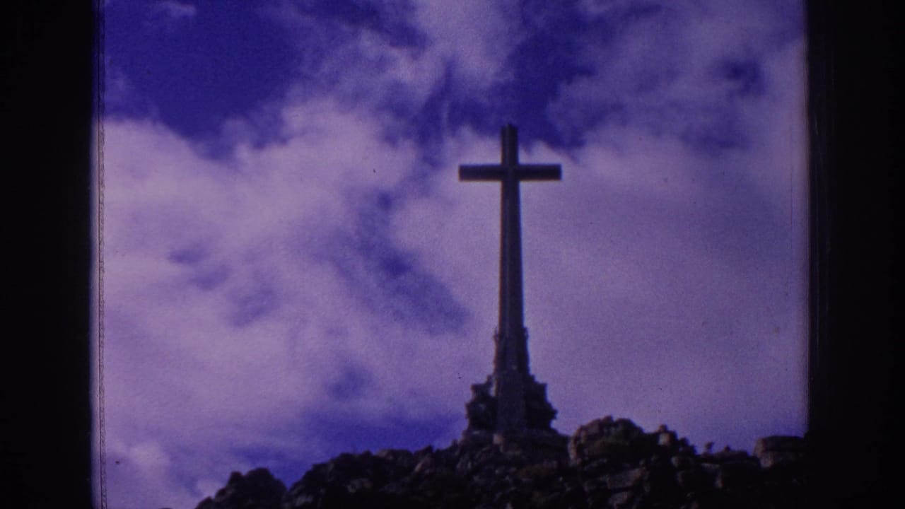 1966 Spain home-movie view of a tall cross monument rising from a rocky hill, framed by dark vertical borders and cloudy sky.