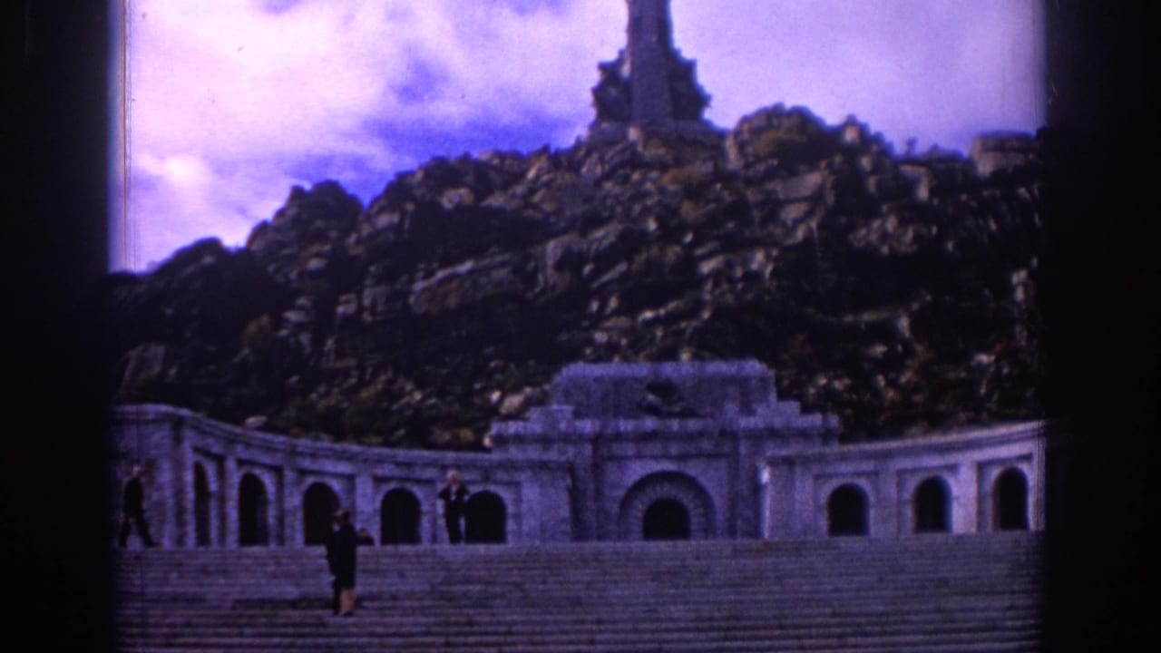 1966 Spain travel footage frame with visitors on massive stairs in front of a colonnaded stone monument beneath rocky terrain.