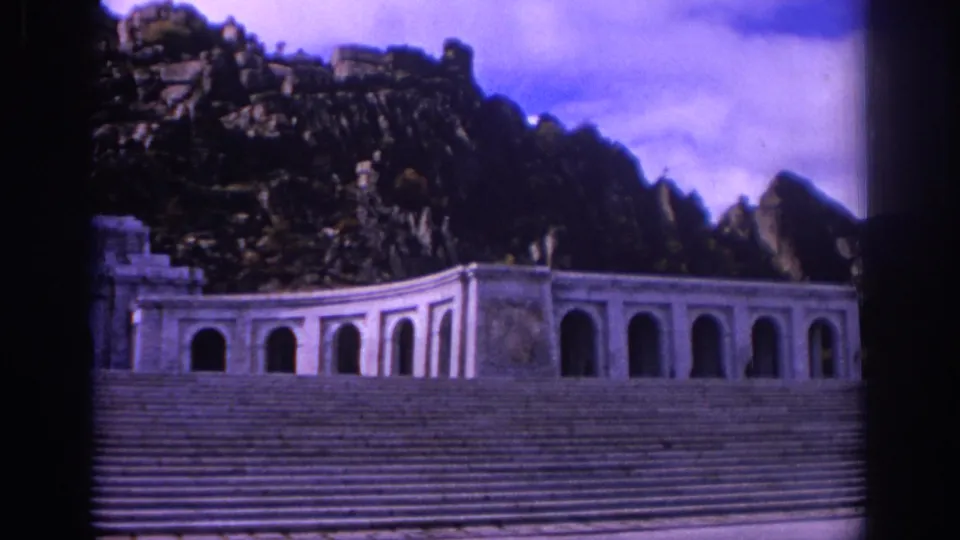 1966 Spain 8mm frame showing a low arched monument facade, expansive stone steps, and rugged rock formations behind.
