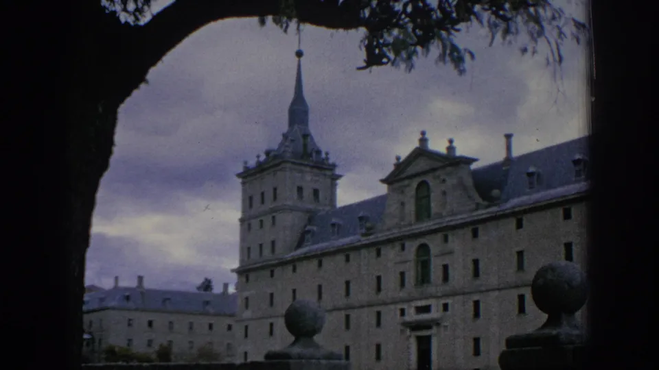 A visitor-shot 1966 Spain frame of the historic complex, with the tower and roofline partly obscured by a foreground tree.
