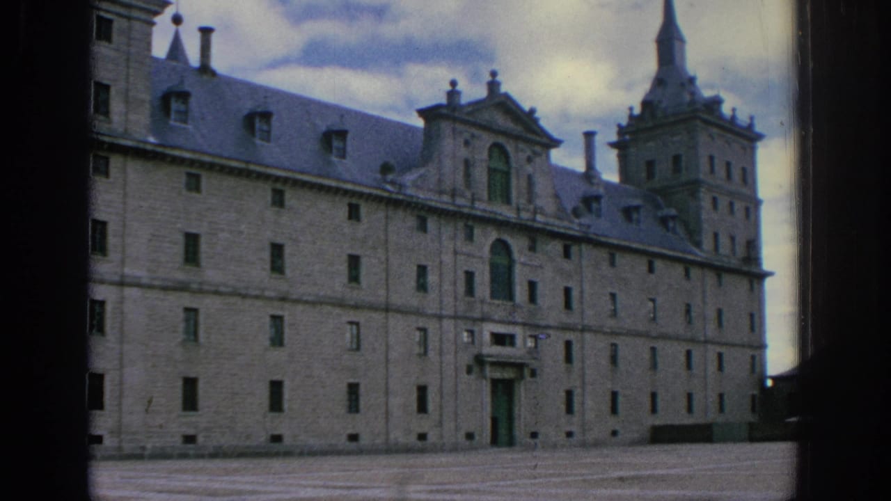 1966 Spain 8mm frame showing a broad exterior view of a historic stone building with slate roof, tower, spire, and empty courtyard.