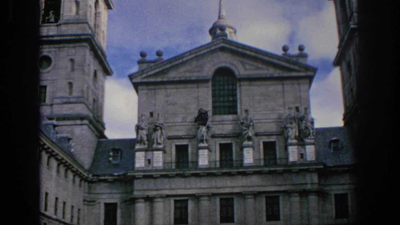 1966 Spain 8mm frame showing a closer view of a historic stone facade with tower, pediment, arched window, statues, and columns.