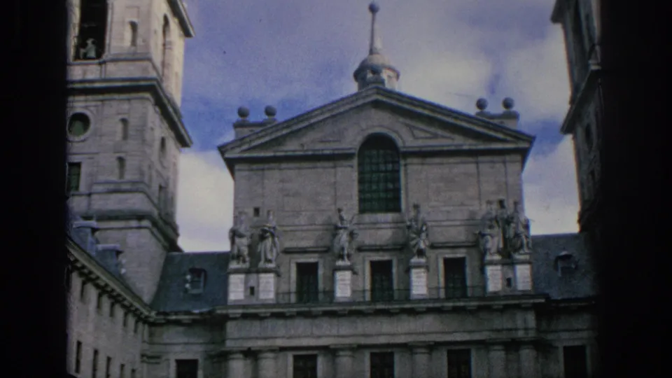 1966 Spain 8mm frame showing a visitor-angle view of the stone facade, tower, arched window, roofline statues, and lower columns.