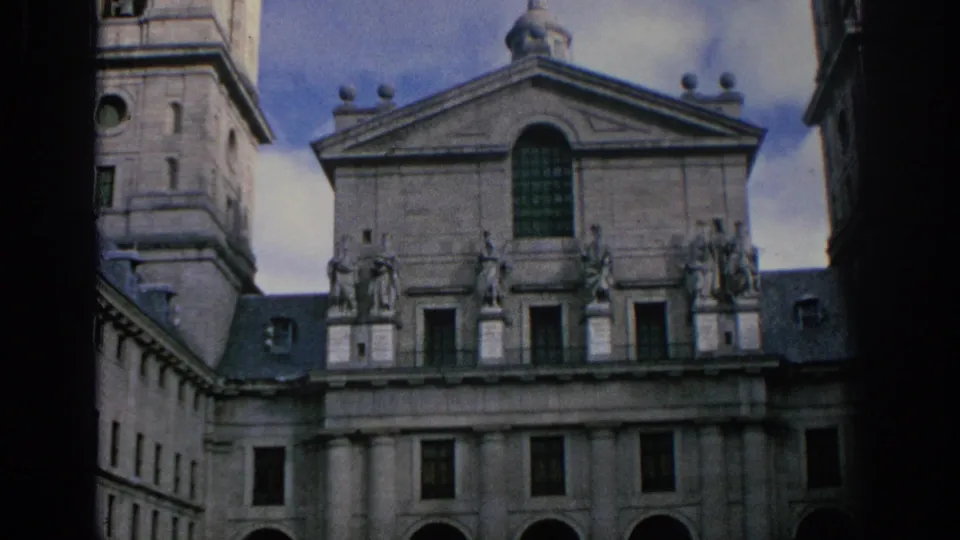 1966 Spain 8mm frame showing the historic stone facade with statues, tower, arched window, lower arches, and visible film-frame edge.