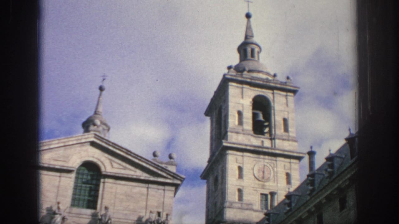 1966 Spain 8mm frame with a bell tower, clock face, arched belfry opening, and part of a historic stone facade.