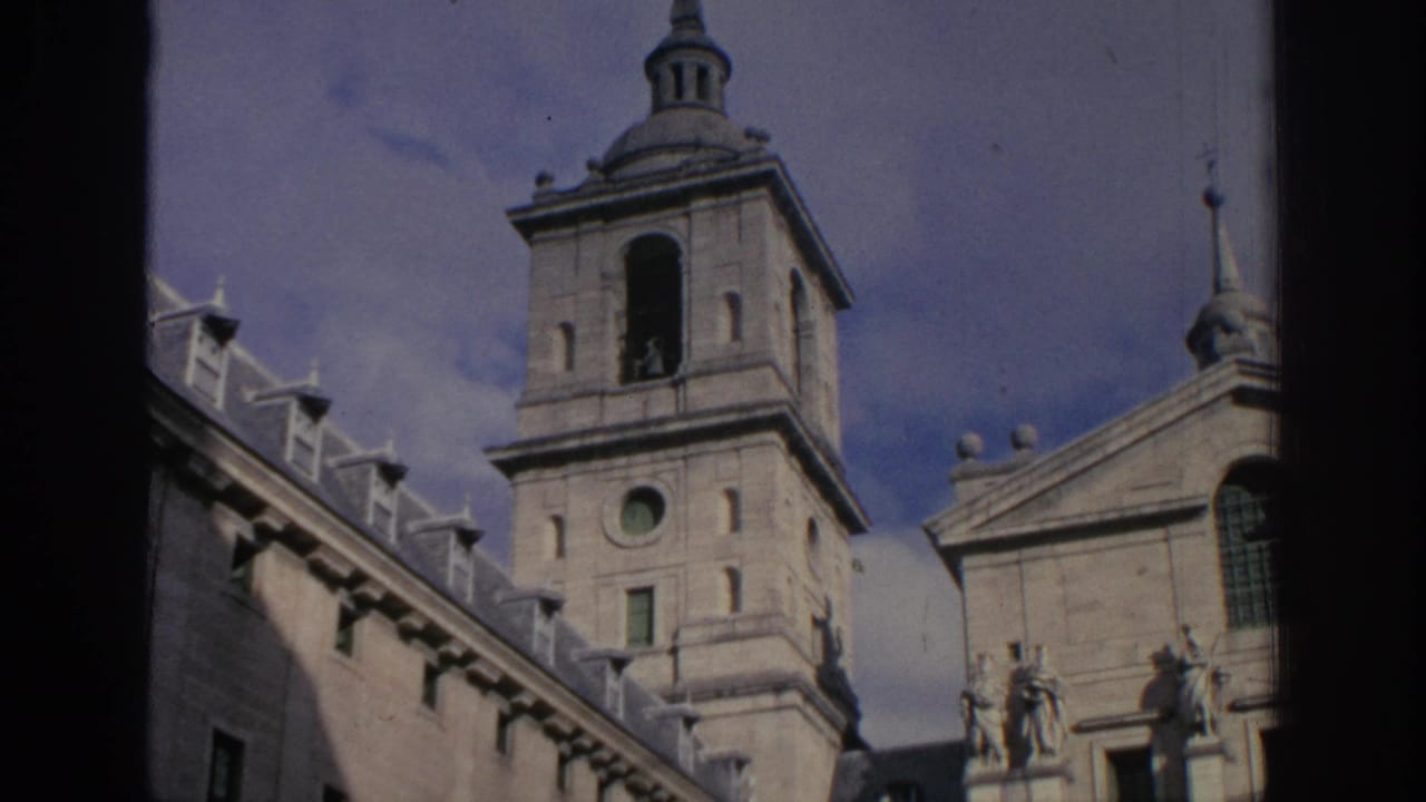 1966 Spain travel footage frame showing a stone bell tower with domed spire beside a classical facade under a pale blue sky.