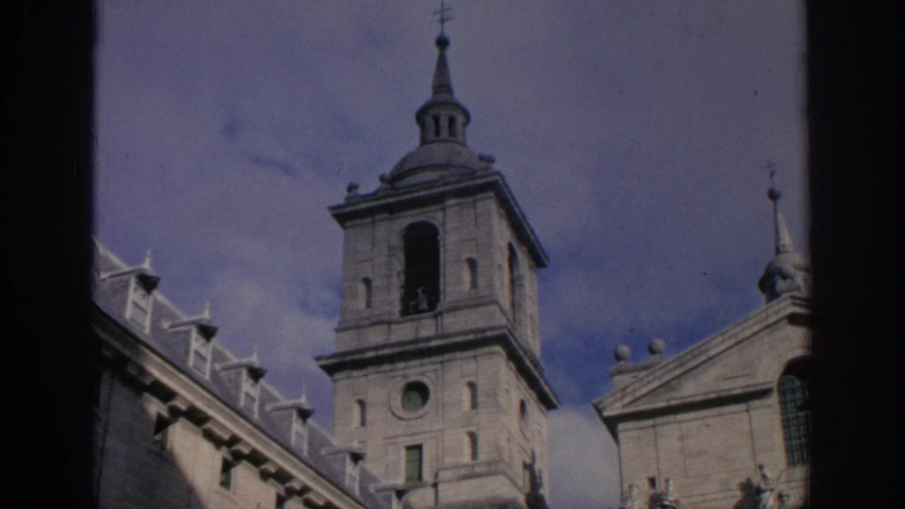 1966 Spain frame with the same historic tower, upper facade, statues or sculptural details, and sky, captured on 8mm film.