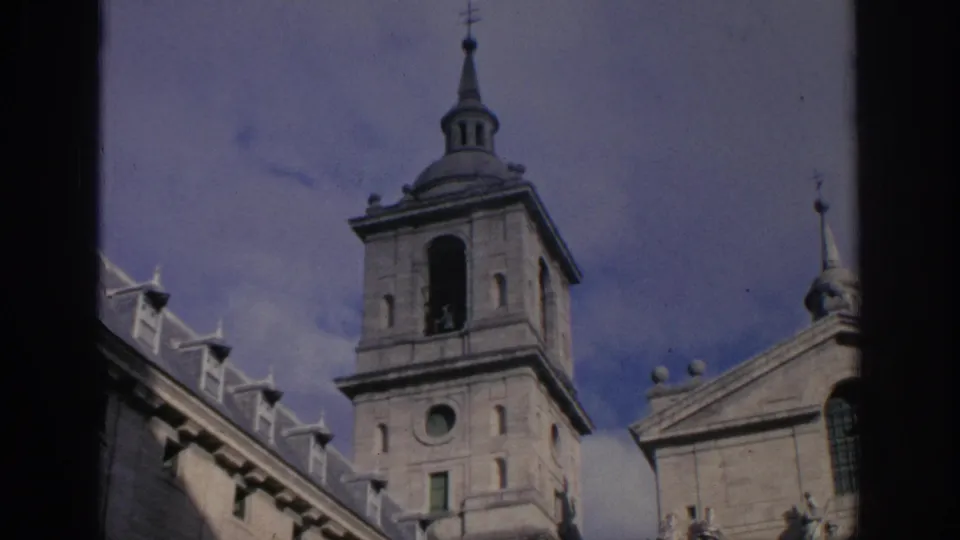 1966 Spain frame with the same historic tower, upper facade, statues or sculptural details, and sky, captured on 8mm film.