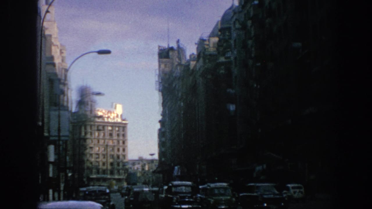1966 Spain street view with classic cars below tall facades and a sunlit block beyond the avenue.