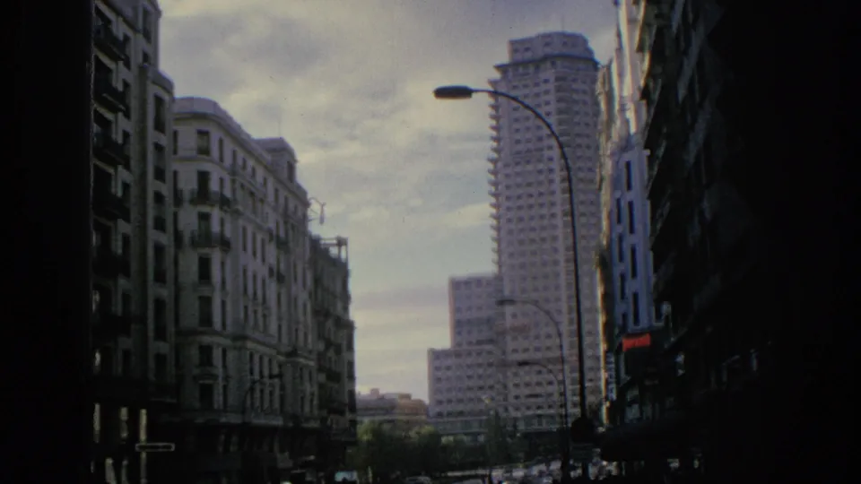 1966 Spain 8mm view of a city street with a distant high-rise, older facades, road traffic, and soft faded color.