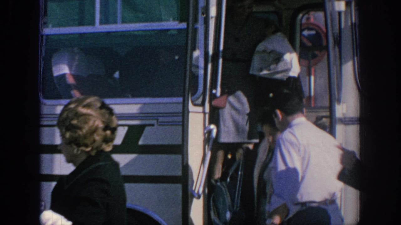 1966 Spain home-movie frame showing people beside a white tour bus, with a man in a light shirt assisting at the open door.