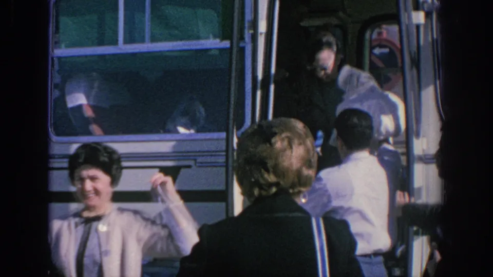 1966 Spain travel footage frame with a smiling woman near a white tour bus as passengers continue boarding or alighting.