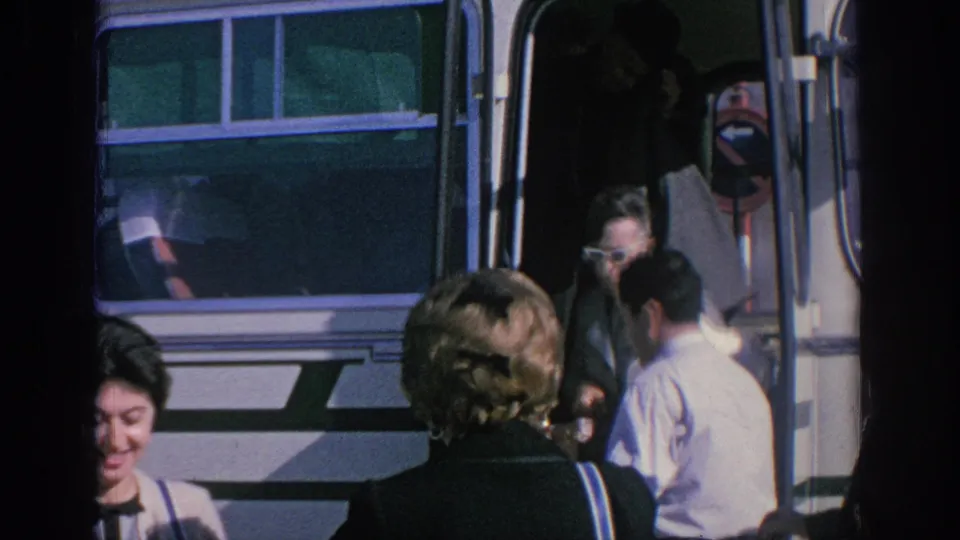 Candid 1966 Spain home-movie frame of passengers by a tour bus, including a smiling woman near the lower edge of the frame.