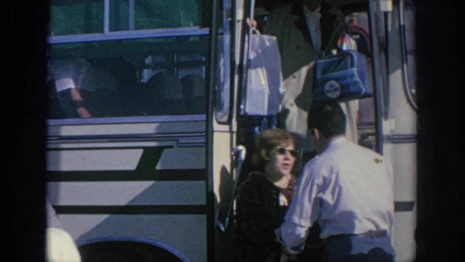 Spain 1966 home-movie frame showing a woman by the bus entrance, luggage near the steps, and a conductor seen from behind.