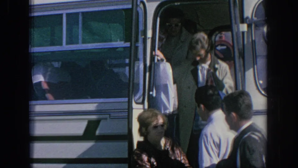 Spain 1966 frame showing adults around a white bus doorway, with the conductor and passengers close together during boarding or alighting.