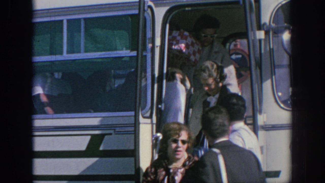 1966 Spain home-movie frame showing adult tourists boarding or leaving a white tour bus in bright sunlight.