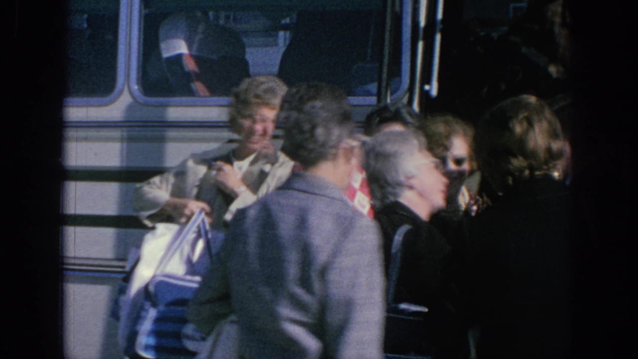 Adult tourists beside a white tour bus in Spain, with visible 1960s clothing, sunglasses, and travel bags.