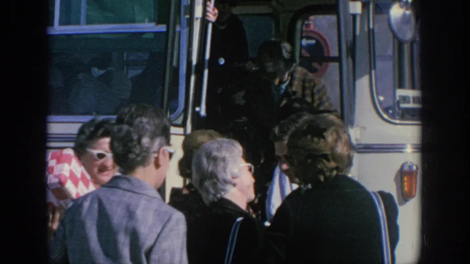 1966 Spain travel frame with tourists at a bus doorway, including visible sunglasses and a red-and-white checkered blanket.