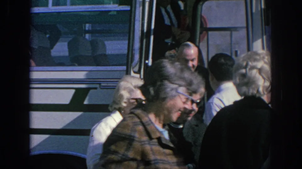 1966 Spain home-movie frame showing older adults clustered near the open doorway of a white bus.
