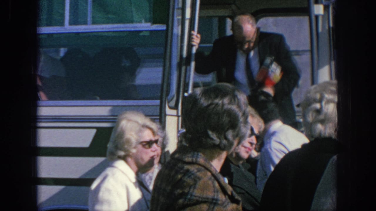 A suited man appears to step from the open bus doorway as older adults wait or pass in front, Spain, 1966.