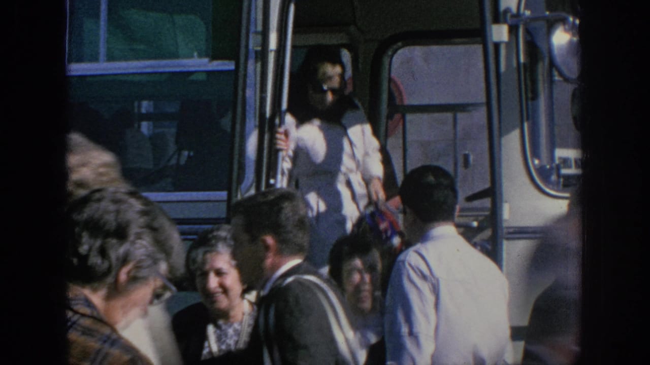 In Spain in 1966, adults in period clothing gather around a white bus while a woman stands at the open doorway.