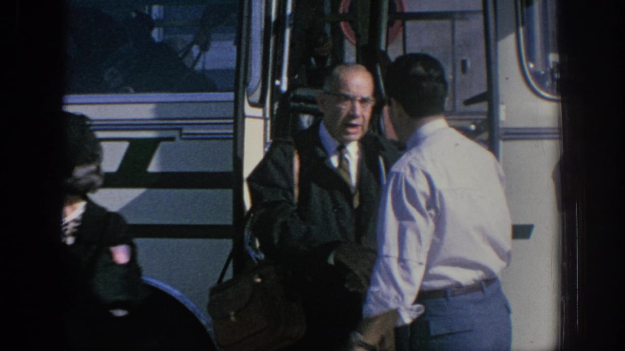 An older man exits a bus while a man in a light shirt faces him.