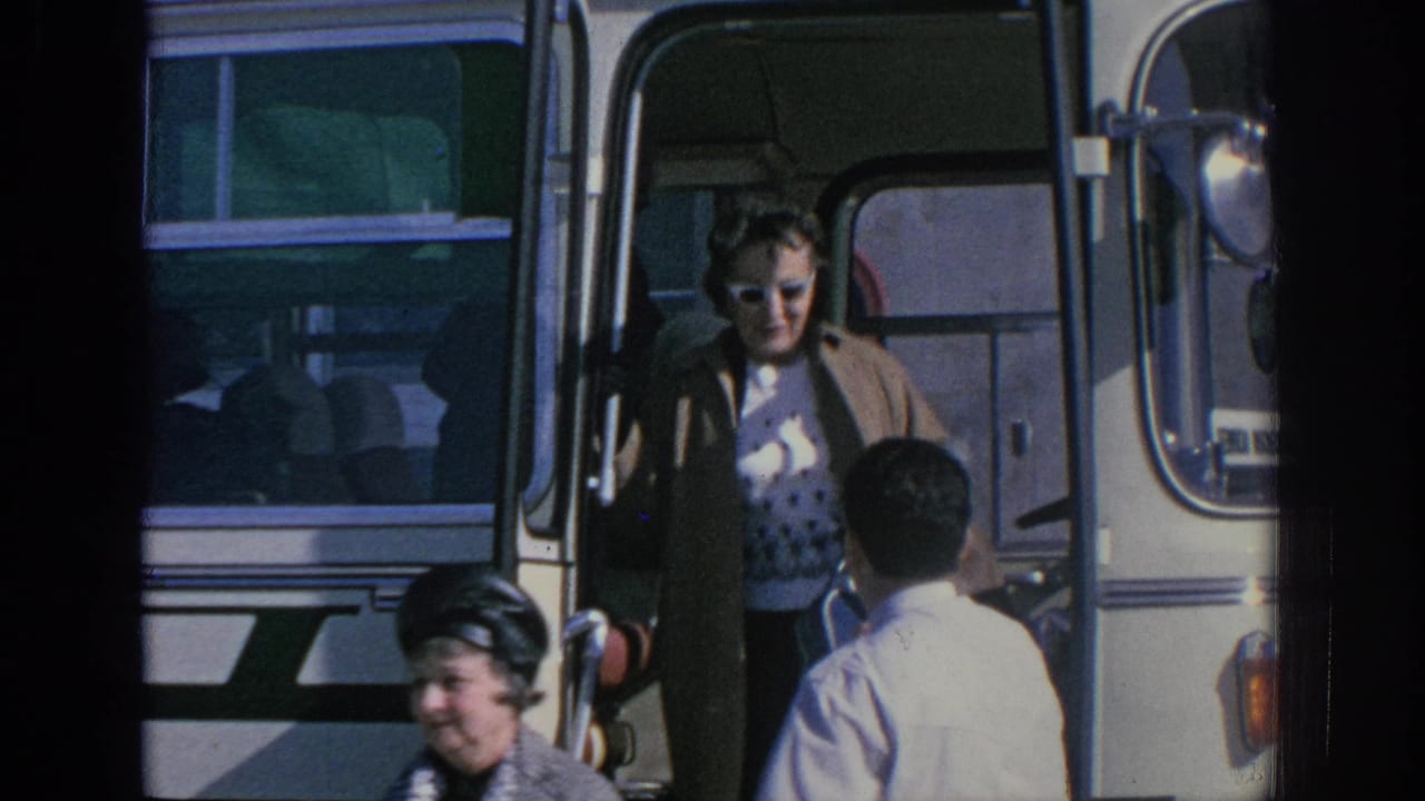 1966 Spain home-movie frame showing adults in sunglasses near the open doorway of a white and green tour bus.