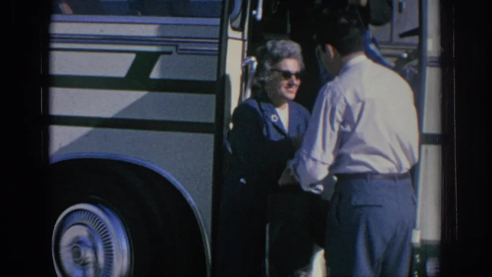 1966 Spain travel frame with a woman in sunglasses beside a striped tour bus and a man seen from behind.