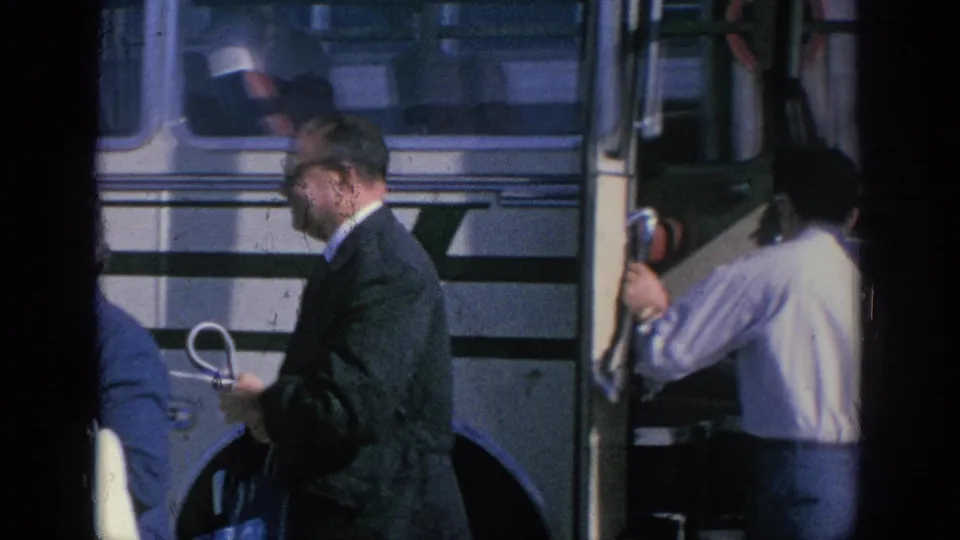 1966 Spain travel frame with a suited adult holding an umbrella beside the striped bus, partly obscured by film-frame shadows.