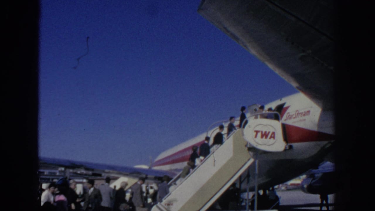 1966 Spain frame with passengers on TWA boarding stairs, aircraft branding, wing shadow, and airport activity in view.