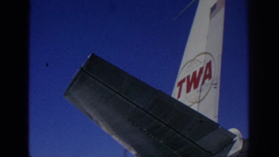 1966 Spain home-movie frame showing the TWA tail logo, American flag marking, and aircraft wing in strong daylight.