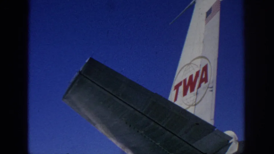 1966 Spain frame focused on the TWA tail, wing underside, and bright sky, with home-movie framing and grain.