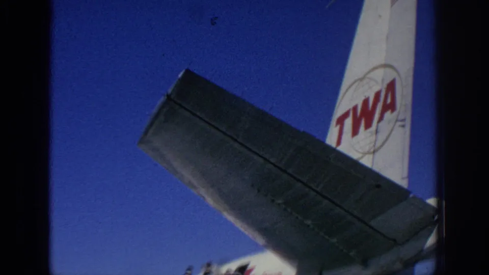 1966 Spain airport footage showing a TWA aircraft tail and wing framed from the tarmac in saturated 8mm color.