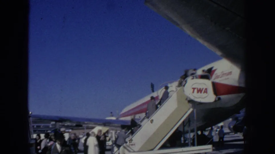 A tarmac crowd gathers near mobile boarding stairs beside a TWA aircraft in 1966 Spain home-movie footage.