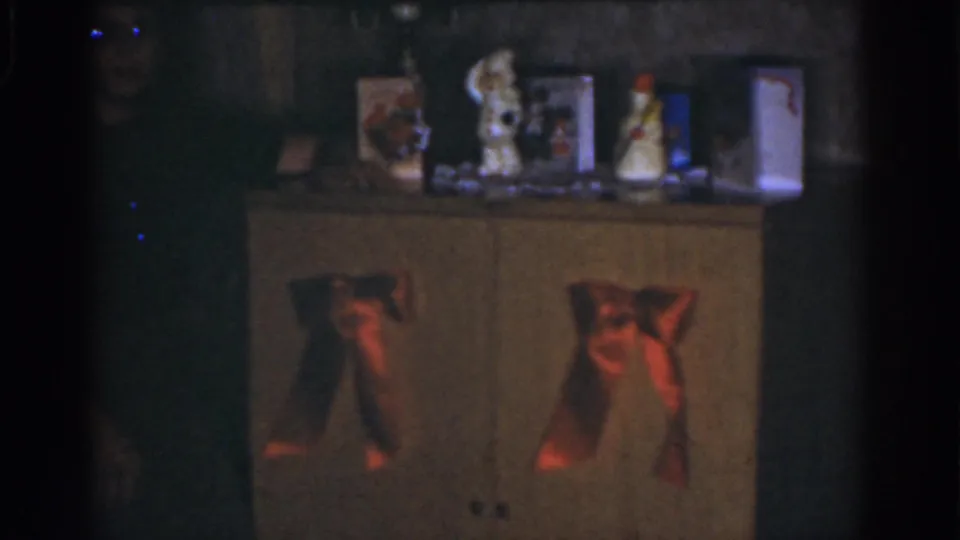 A 1968 Omaha holiday interior shows a cabinet with red bows and tabletop Christmas decor while a woman is partly visible in shadow.