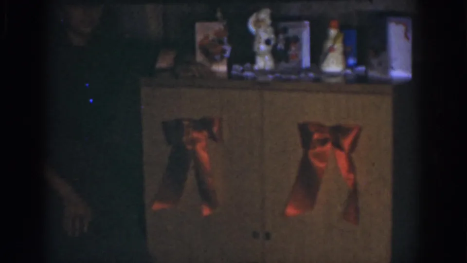 Dim 1968 Omaha interior with a decorated cabinet, tabletop ornaments, red bows, and a person partly visible beside it.