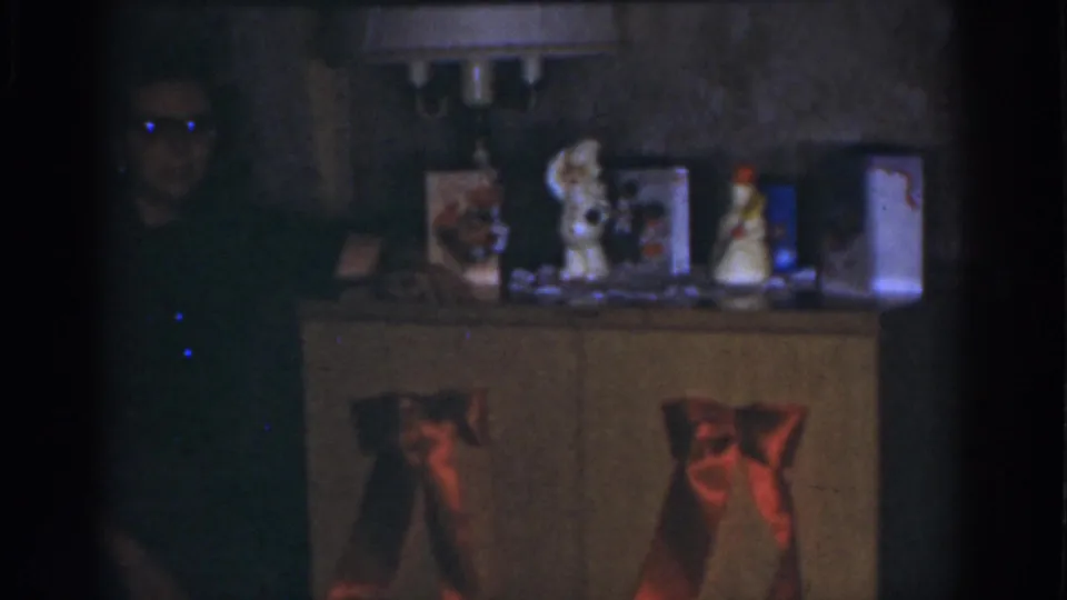 Soft 8mm frame from a 1968 Omaha home interior showing a holiday-decorated cabinet and a dark figure near the edge.